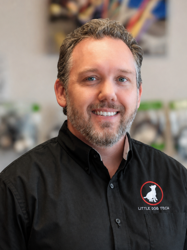Smiling man with gray hair and beard, wearing a black shirt with the Little Dog Tech logo (white dog inside a red circle).